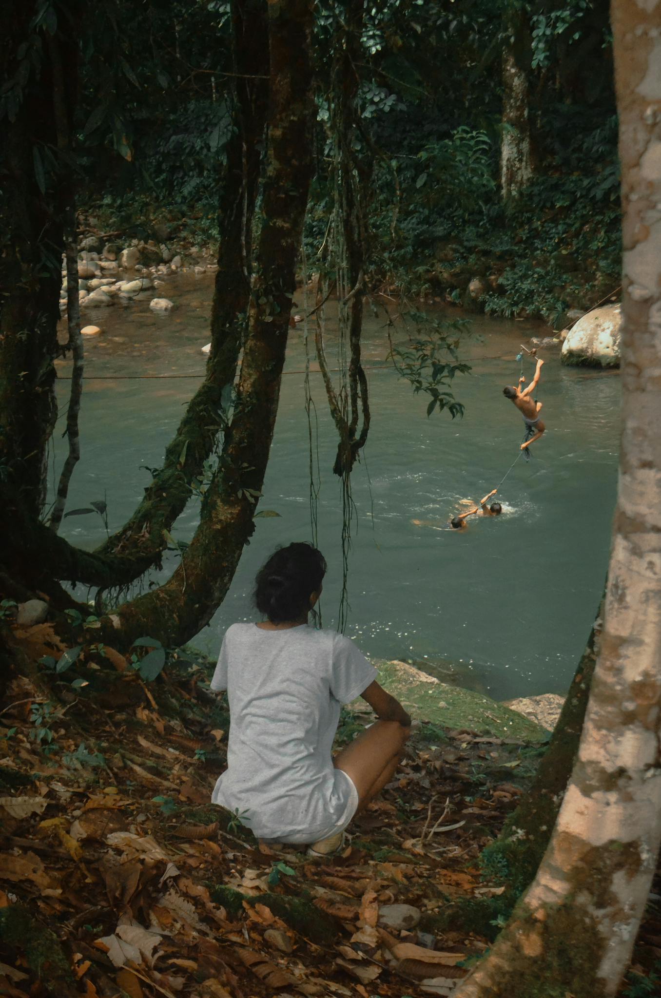 From above back view of anonymous female resting on hill near children having fun in pond